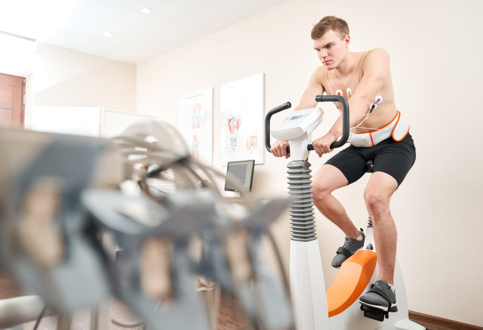 Man patient, pedaling on a bicycle ergometer stress test system for the function of heart checked. Athlete does a cardiac stress test in a medical study, monitored by the doctor