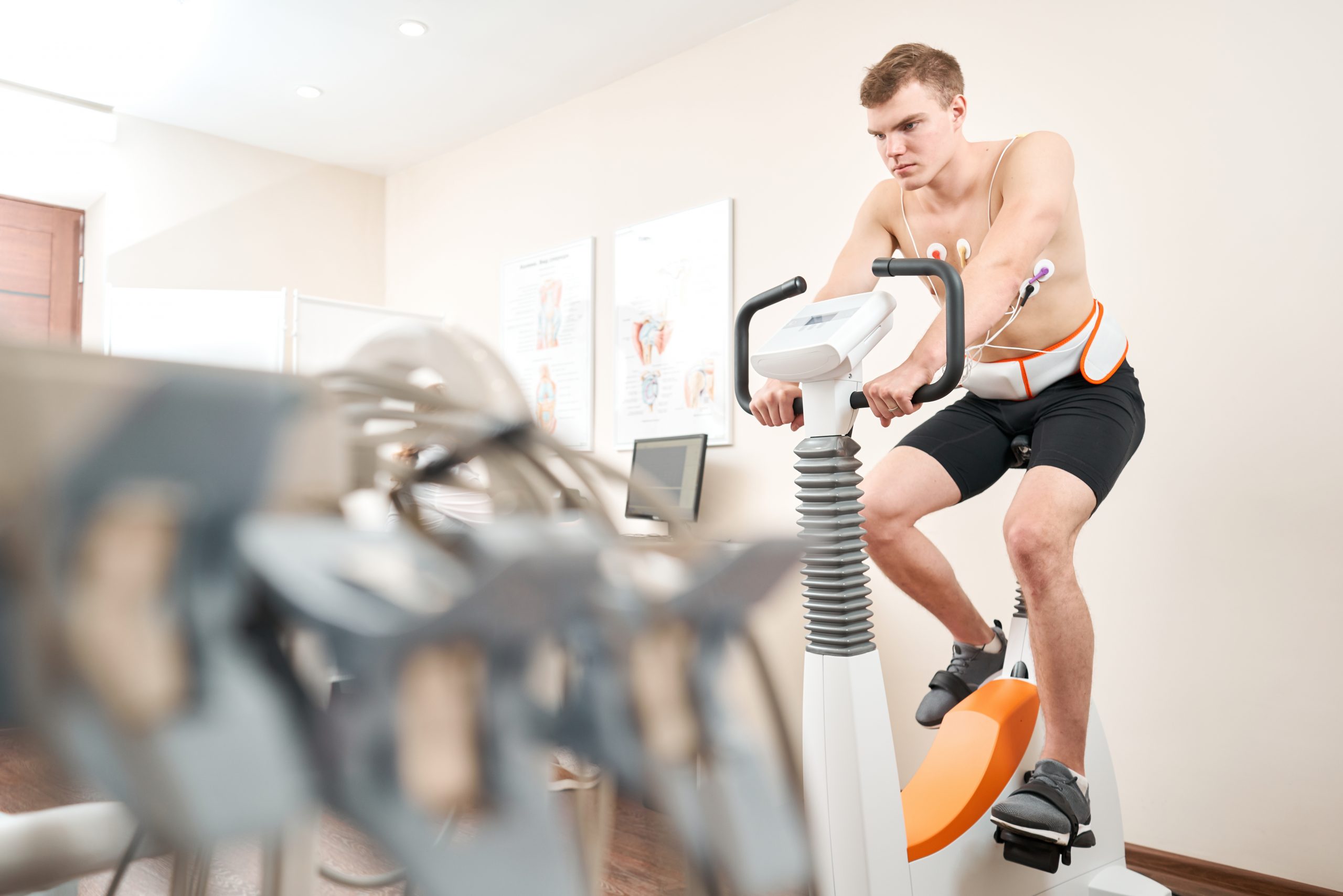 Man patient, pedaling on a bicycle ergometer stress test system for the function of heart checked. Athlete does a cardiac stress test in a medical study, monitored by the doctor