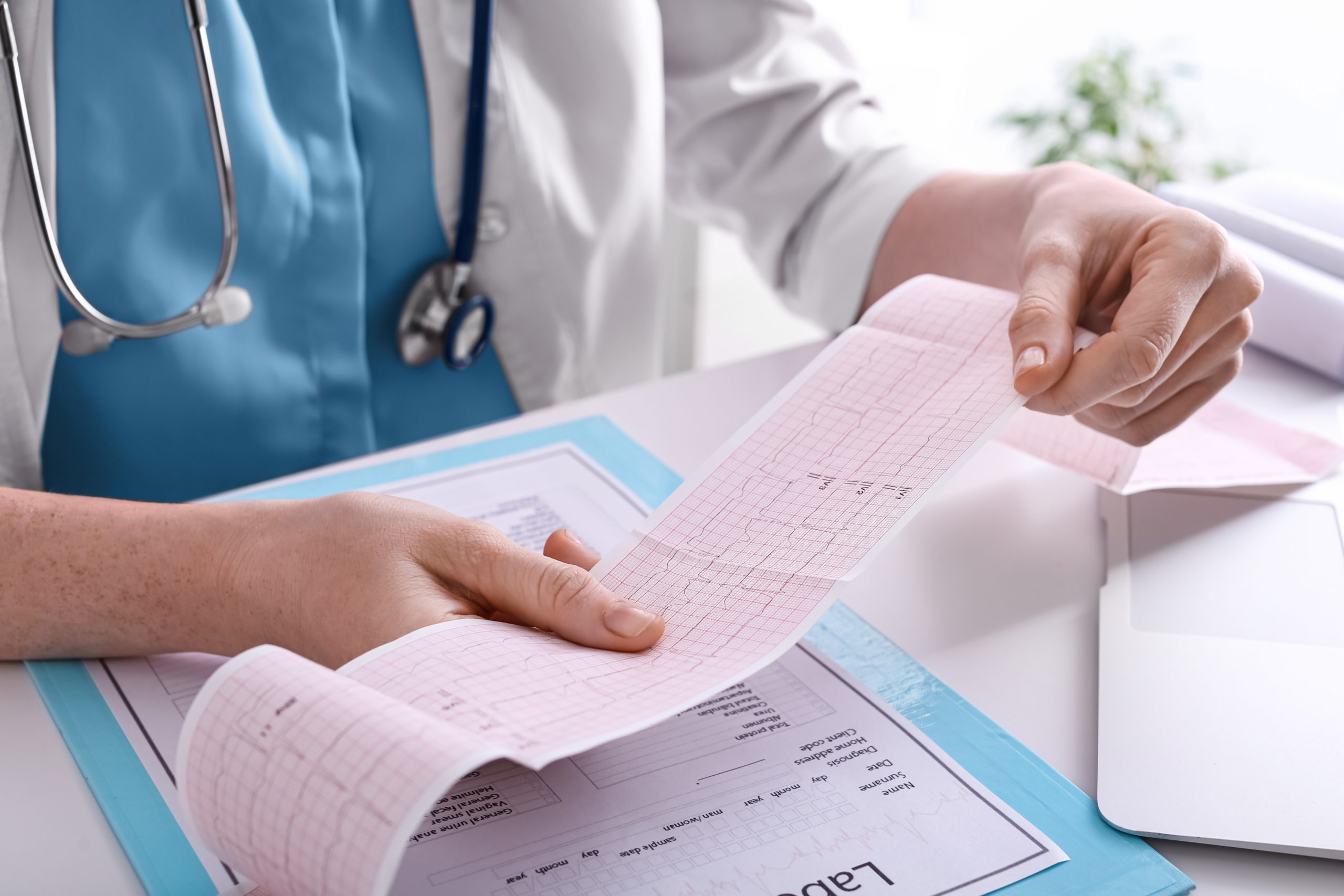 Doctor examining cardiogram at table in clinic, closeup