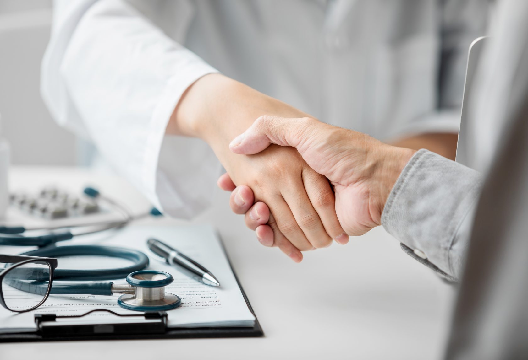 Close up of female Doctor and patient shaking hands after discussing and consulting with a patient in an examination room at a hospital, Medical and Health Care Concept.